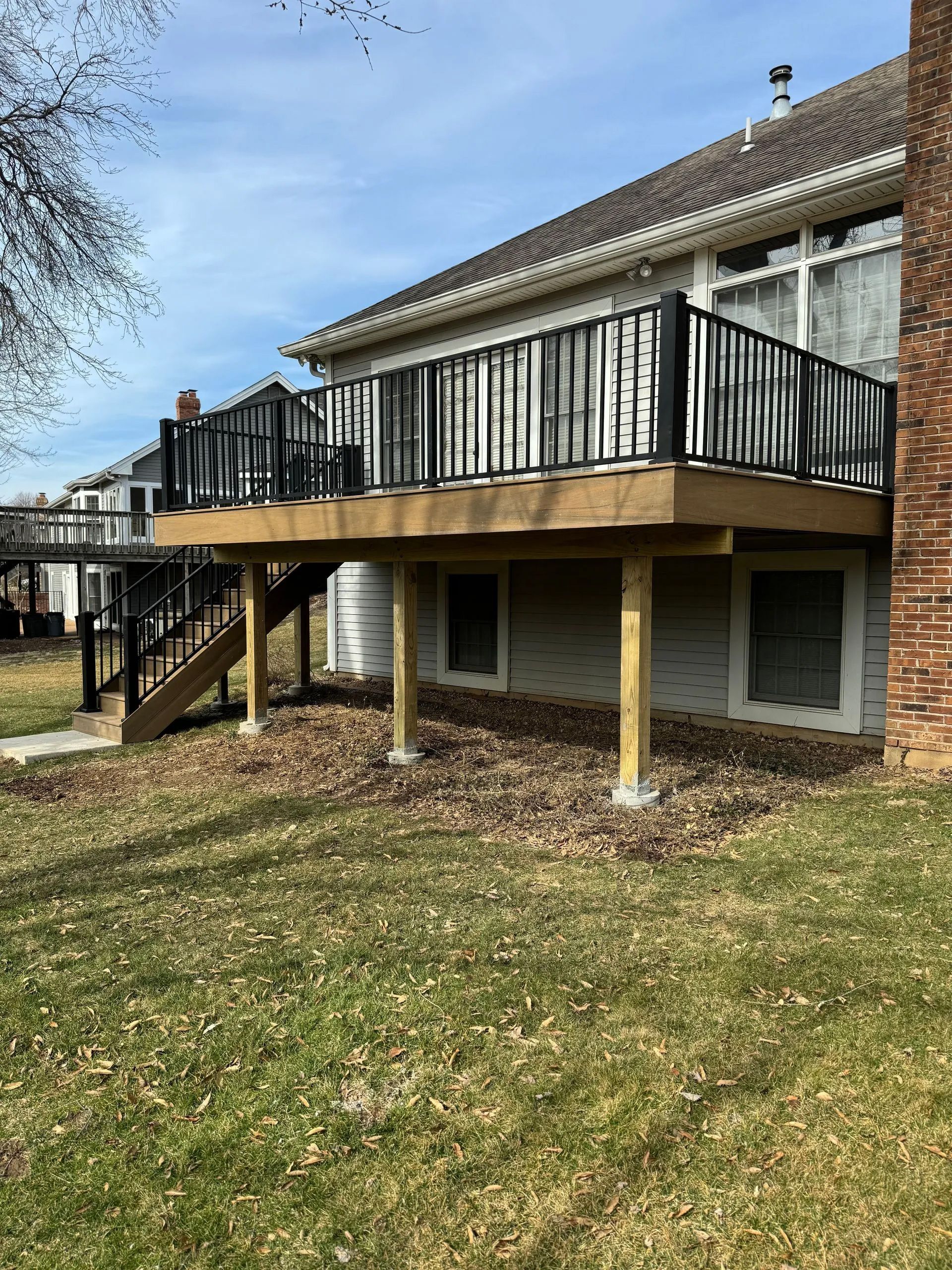 A large wooden deck with a black railing is in the backyard of a house.