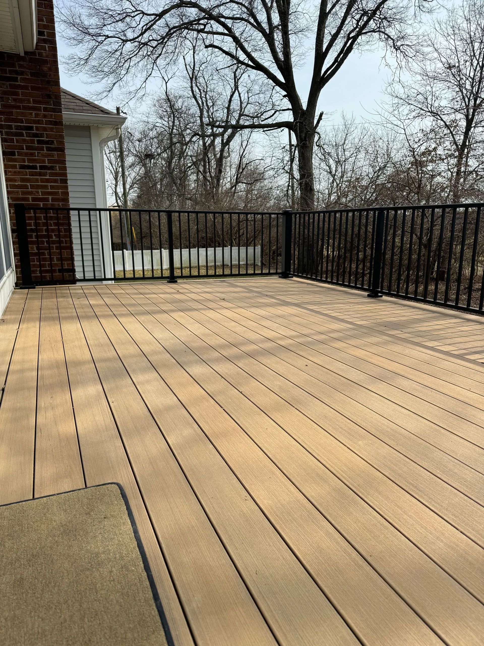 A wooden deck with a metal railing and trees in the background.