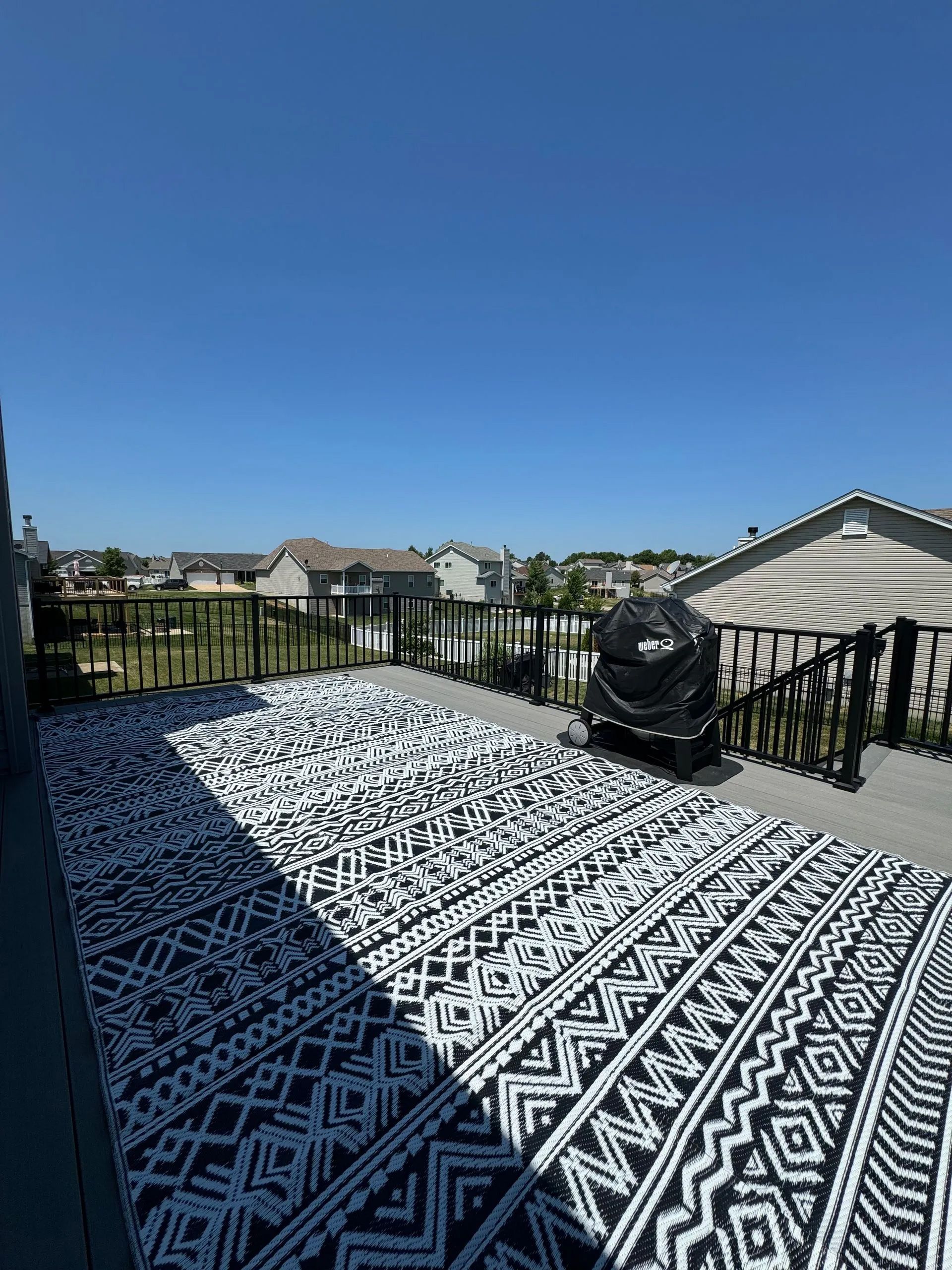 A black and white rug is on a balcony with a view of a city.