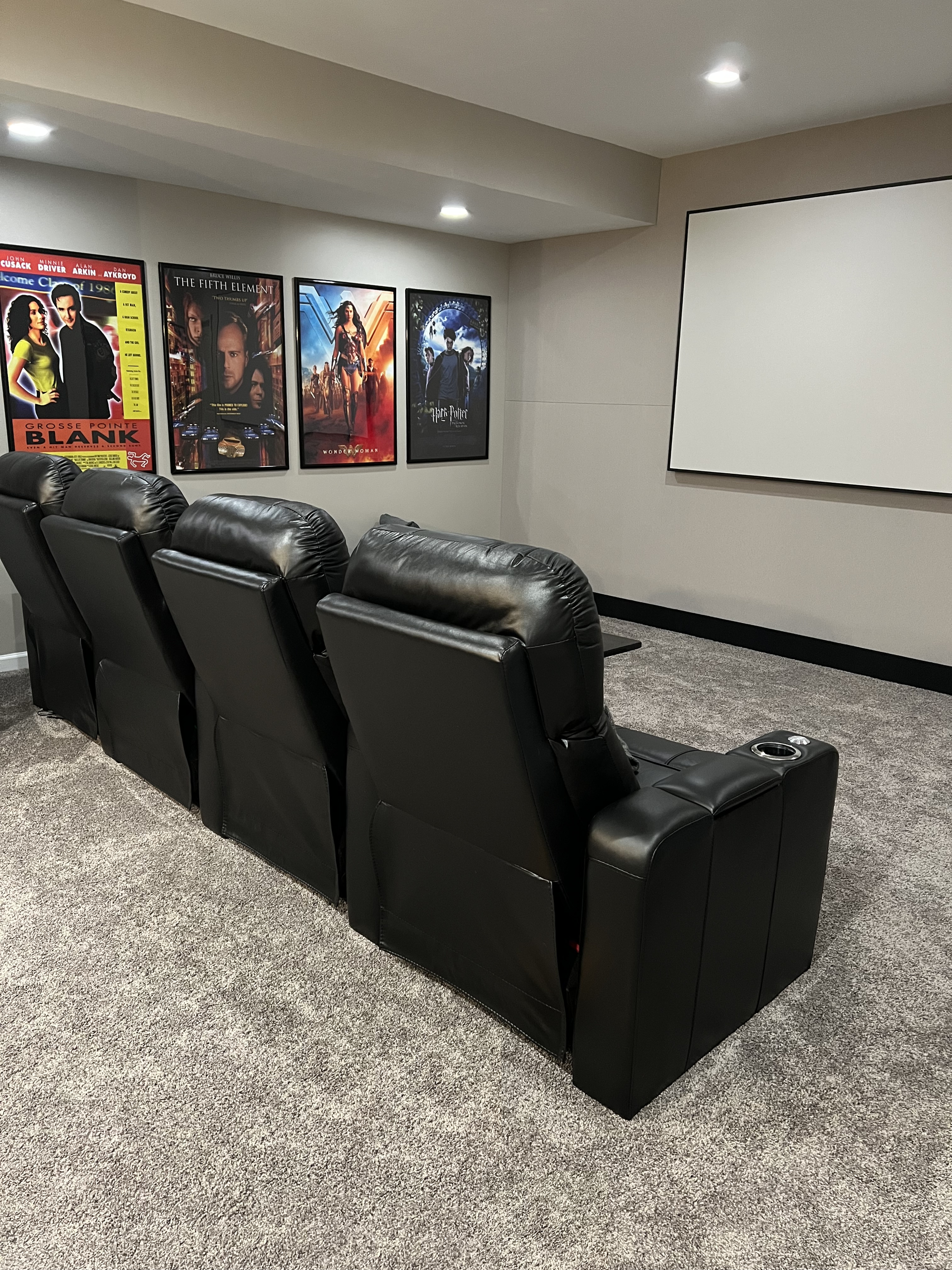 A home theater with a projector screen, chairs, and posters on the wall.