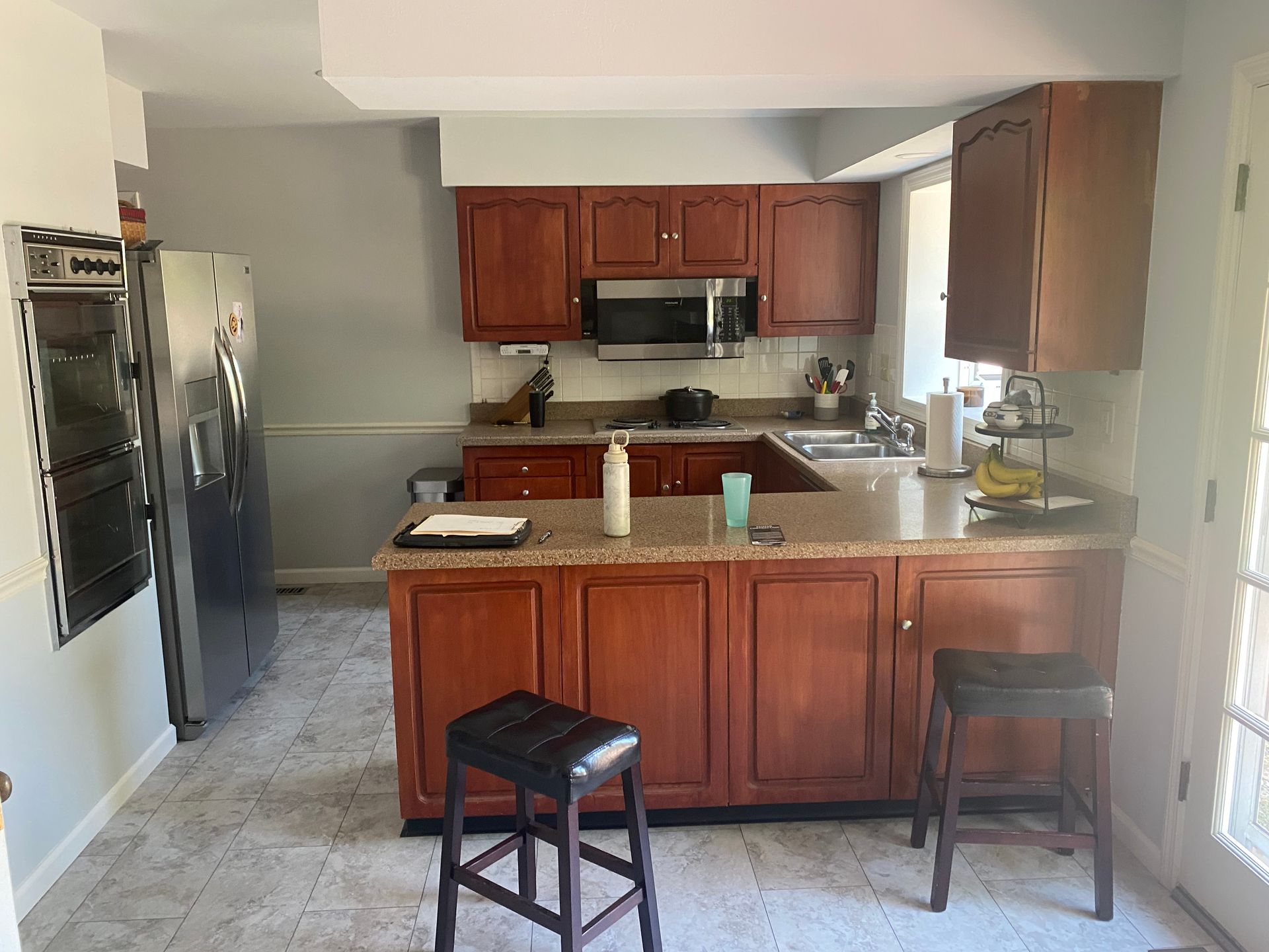 A kitchen with wooden cabinets, granite counter tops, stools, and a refrigerator