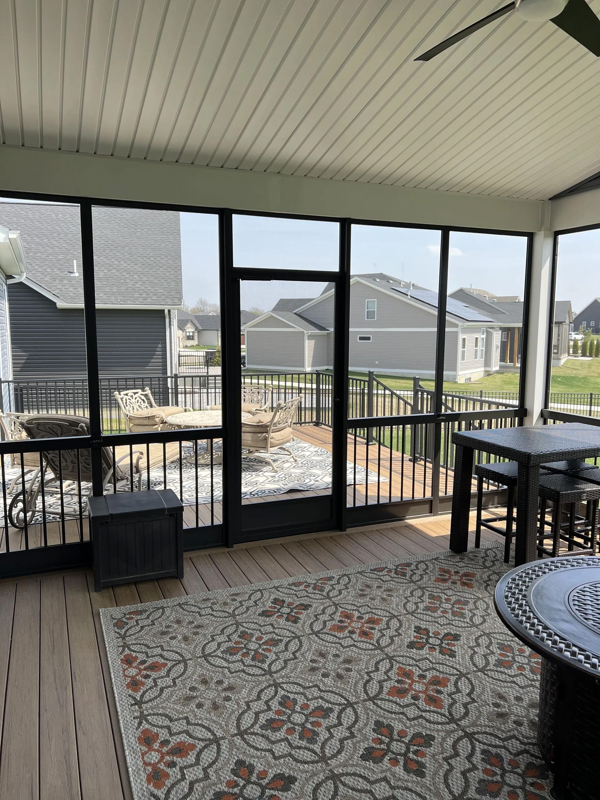 A screened in porch with tables and chairs and a ceiling fan.