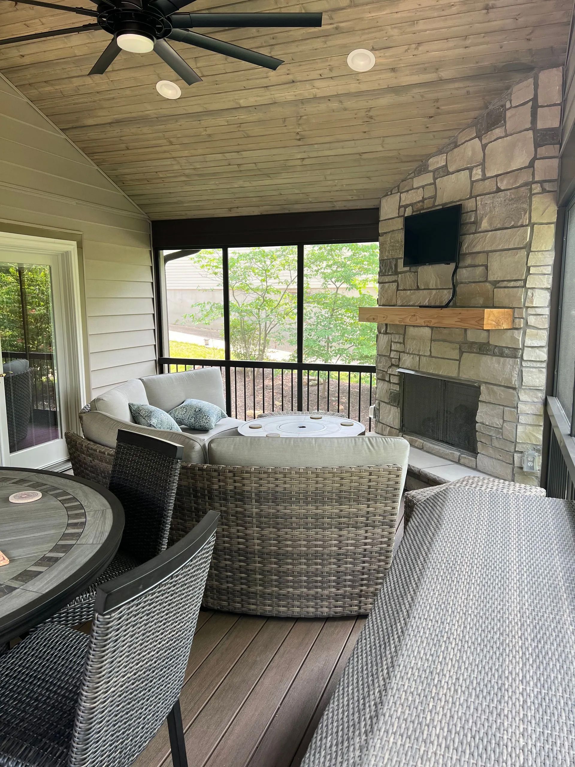 A screened in porch with a fireplace and a ceiling fan.