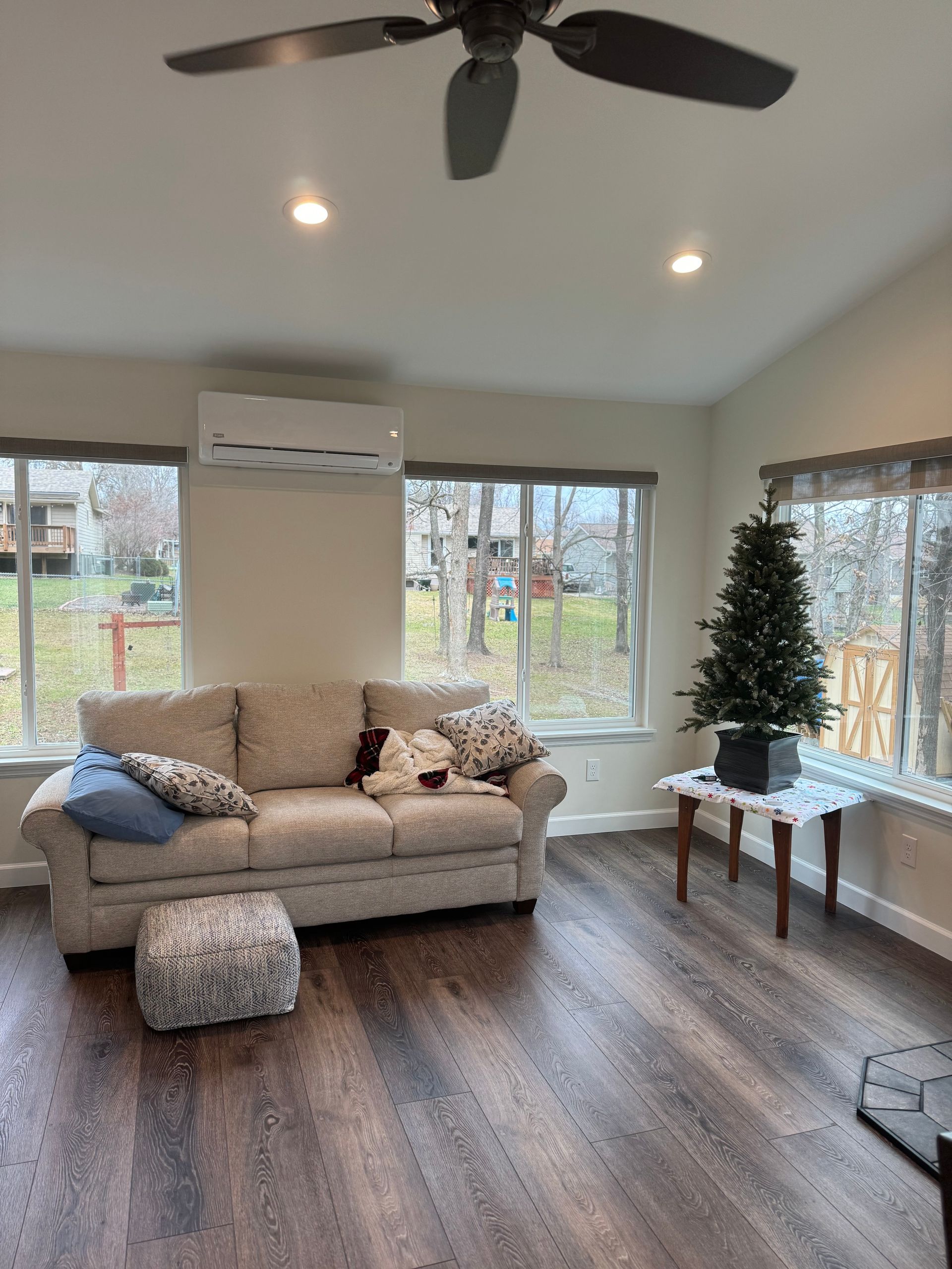 A living room with a couch, ottoman, ceiling fan and a christmas tree.