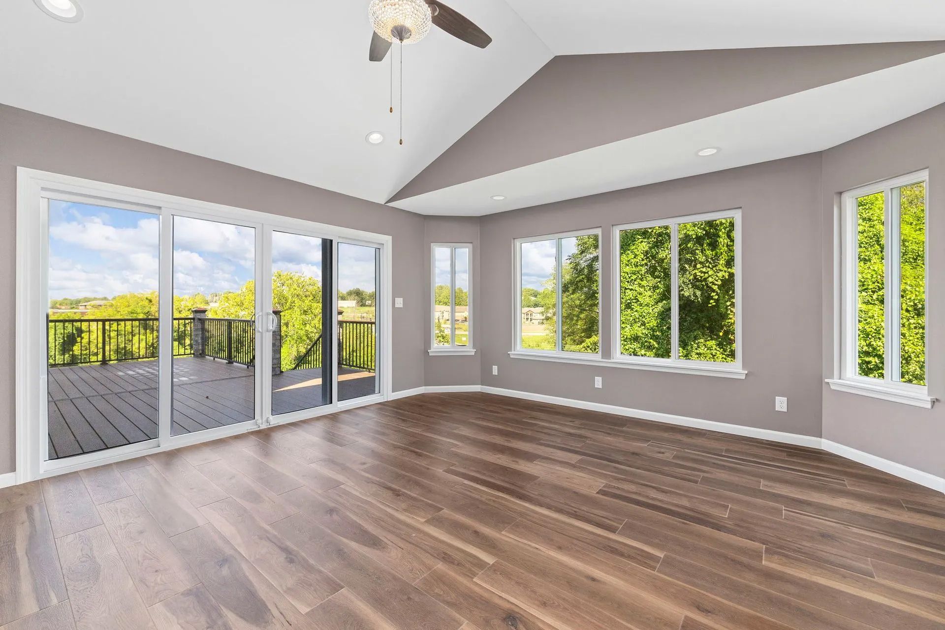 An empty living room with hardwood floors, sliding glass doors, and a ceiling fan