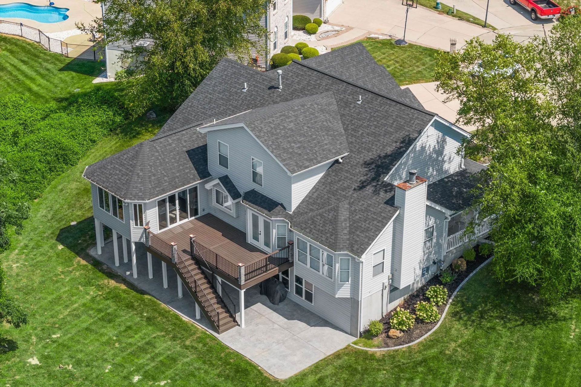 An aerial view of a large white house with a black roof and a large deck.