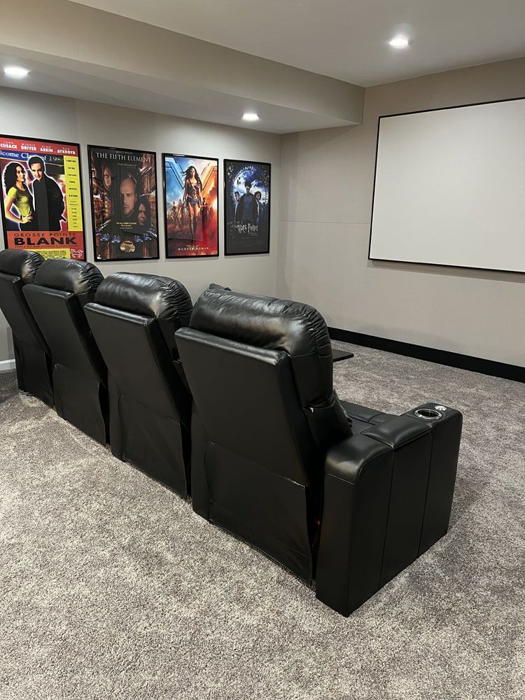 A home theater with a projector screen, chairs, and posters on the wall