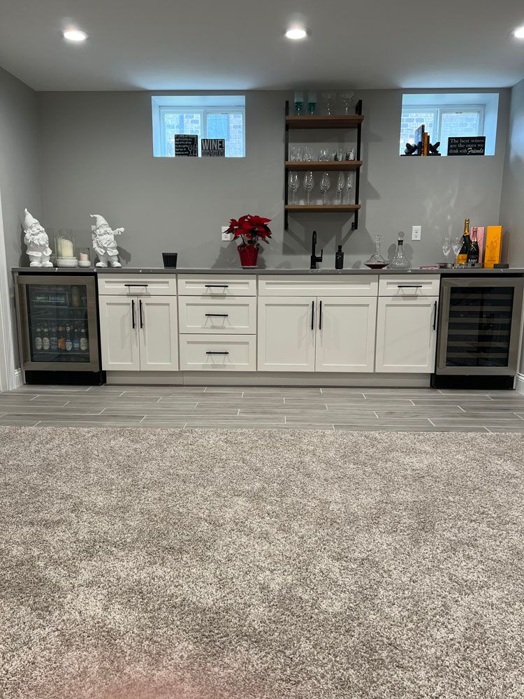 A basement bar with white cabinets, a refrigerator, and a sink