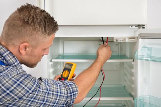 Man in plaid shirt using a multimeter to test the light in a refrigerator.