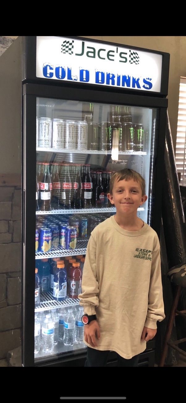 Teen standing in front of a refrigerated drink cooler at Jace’s Gold Drinks with assorted beverages inside