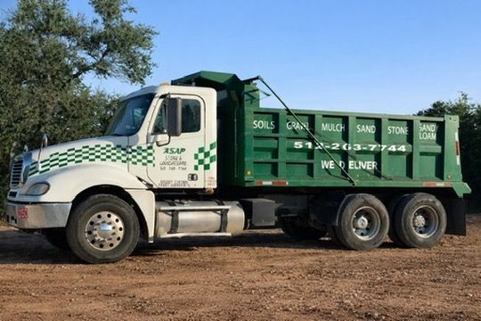 Green garbage truck parked on dirt road under a clear sky