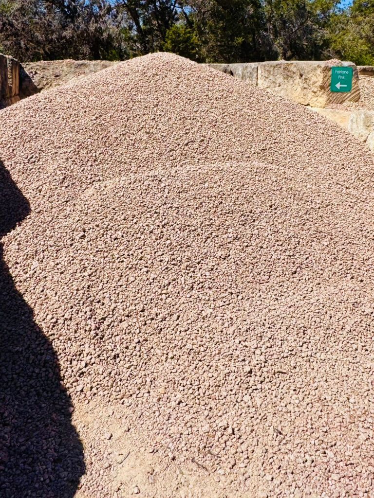 Large pile of light-colored gravel outdoors beside a dirt path and a small green sign