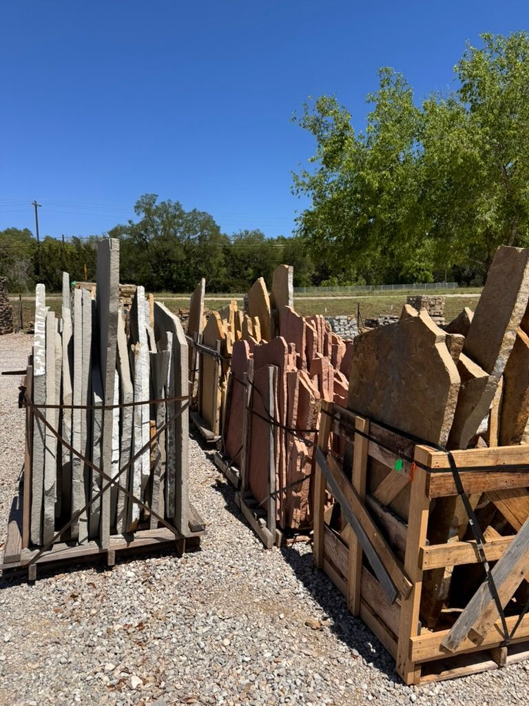 Stacked stone slabs in wooden pallets on gravel outdoors under a clear blue sky