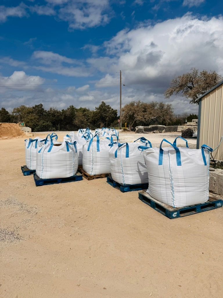 White industrial bags on blue pallets in a dusty outdoor yard under a cloudy sky