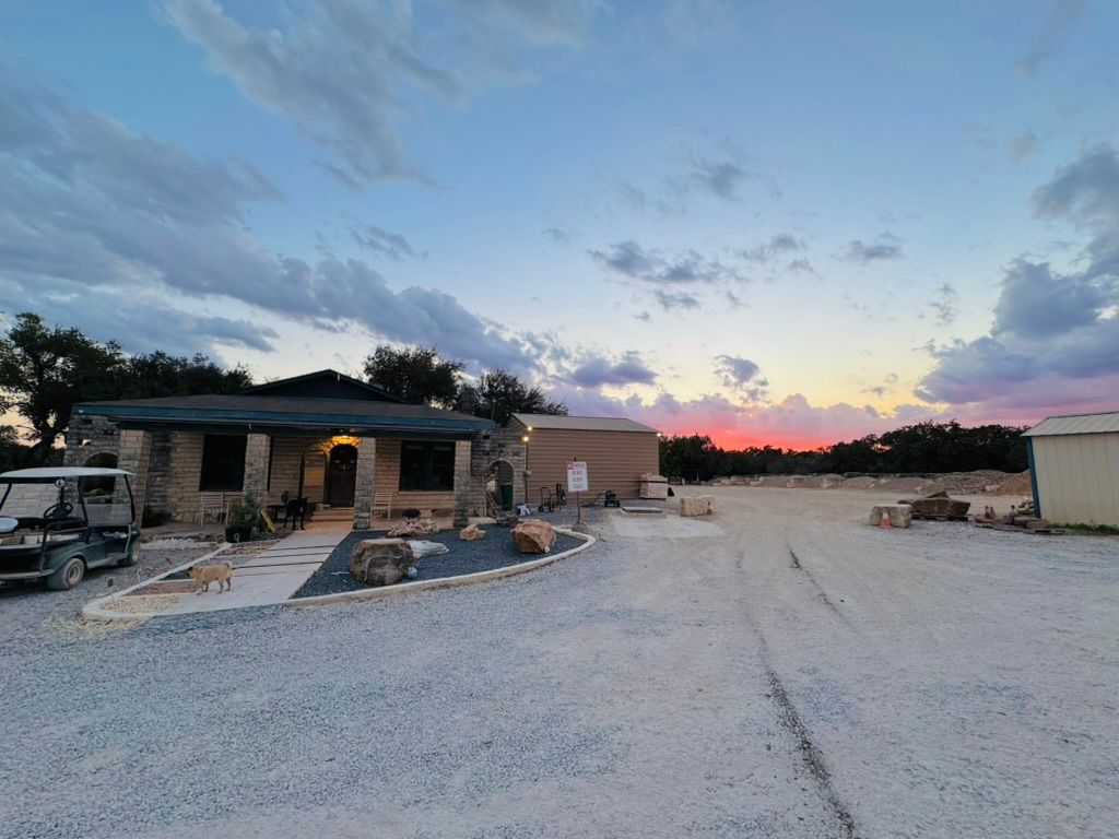 Small stone house and gravel driveway at sunset under a blue and pink sky