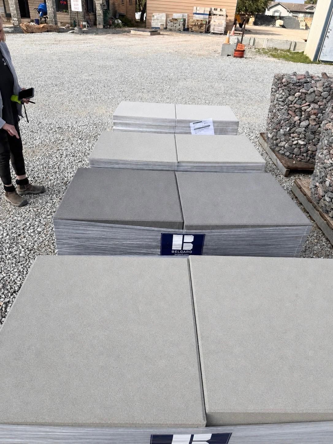 Stacked gray stone slabs in an outdoor yard, with a person standing at the left edge.