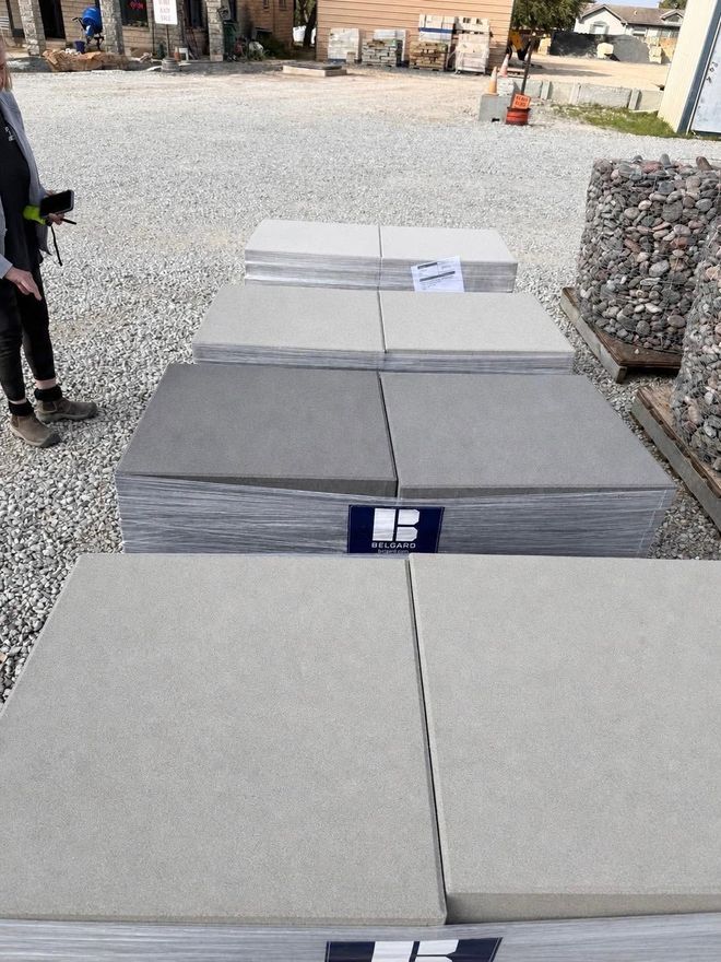 Stacked gray stone slabs in an outdoor yard, with a person standing at the left edge.