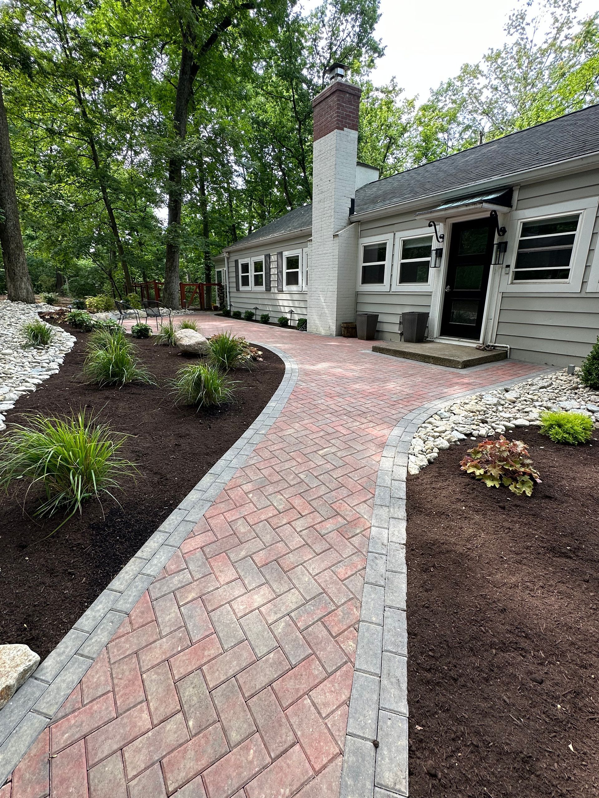 A brick walkway leading to a house with a chimney.