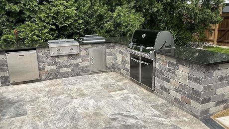 A large outdoor kitchen with a grill and a brick wall.