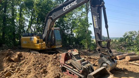 A deere excavator is digging a hole in the dirt.