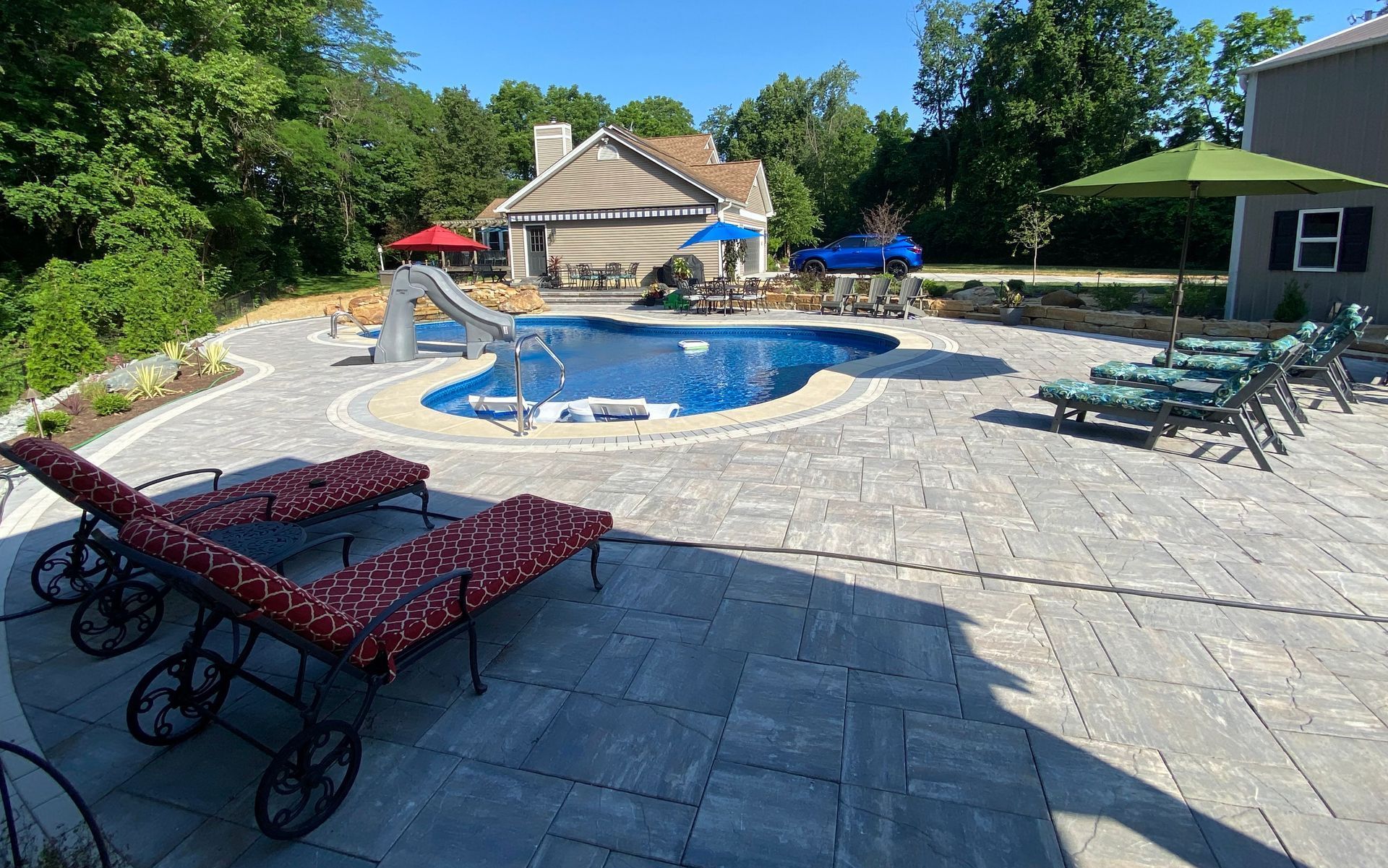 A large swimming pool is surrounded by chairs and umbrellas on a patio.