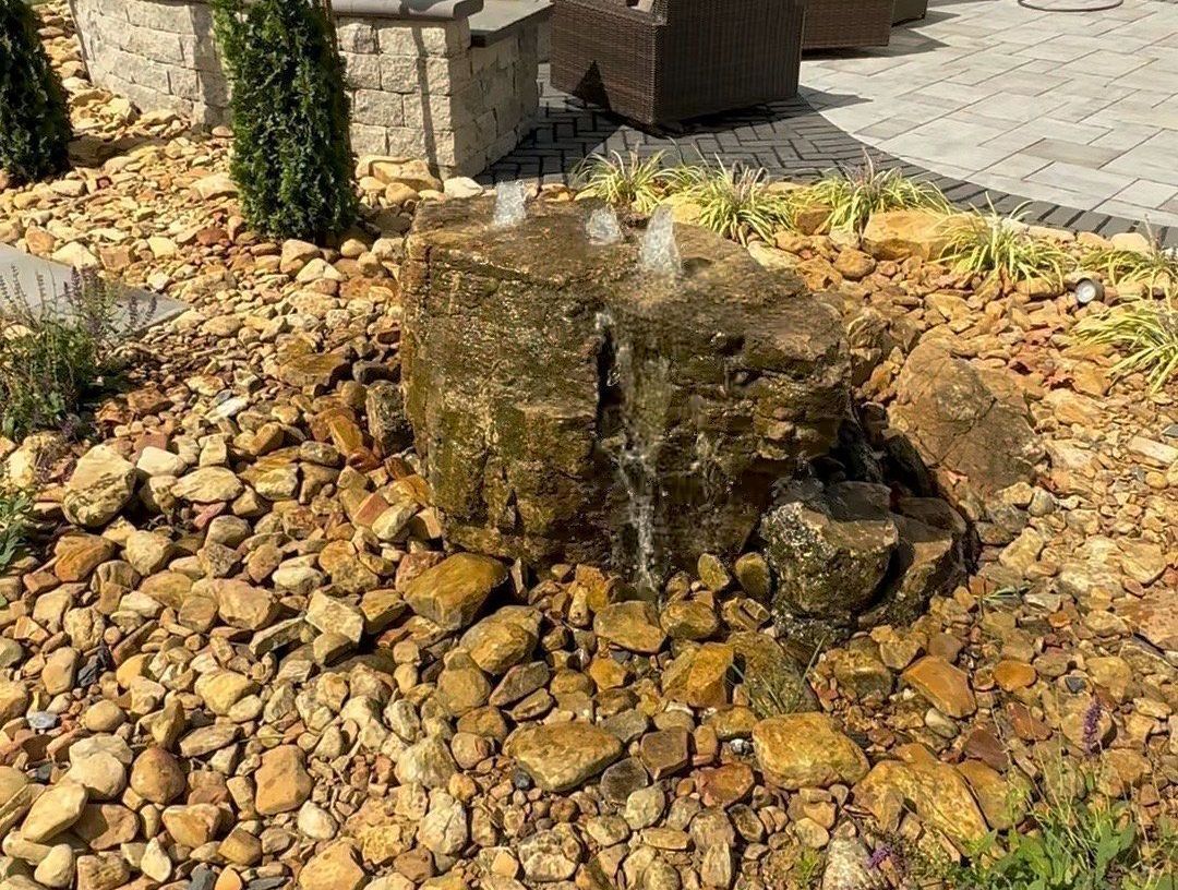 There is a fountain in the middle of the rocks in the backyard.