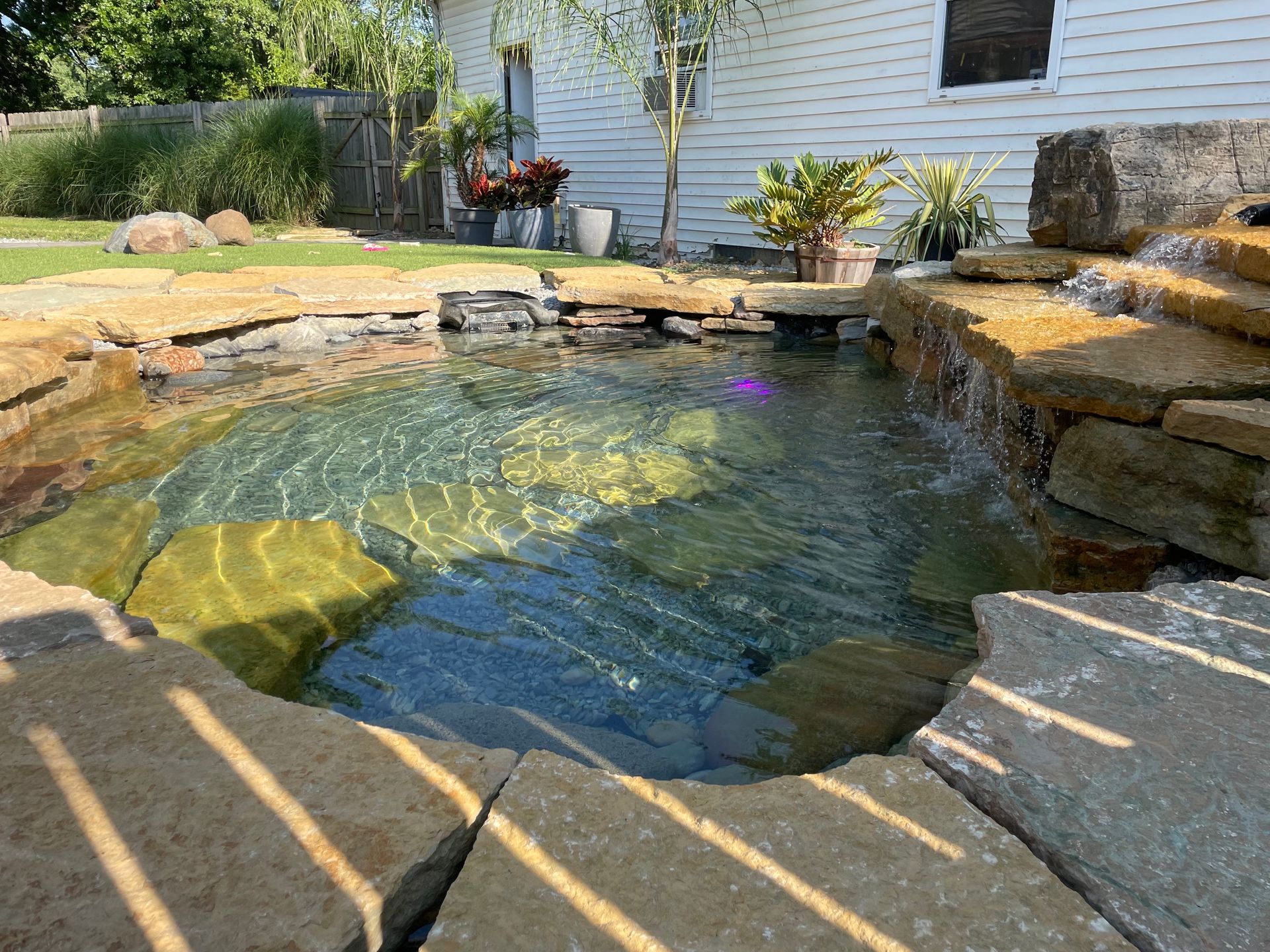 A pond with a waterfall in the backyard of a house.