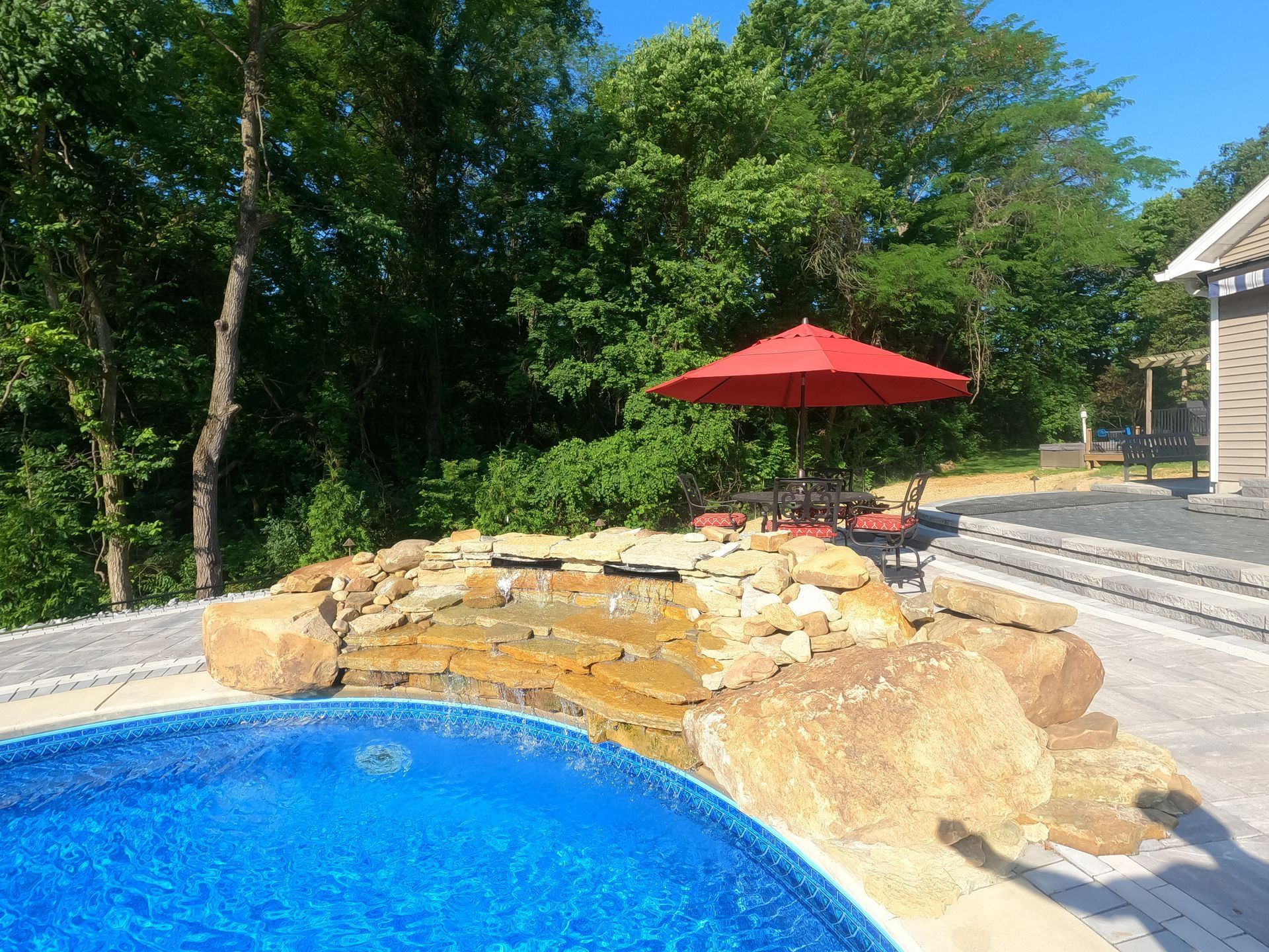 A swimming pool with a red umbrella and a waterfall in the background.