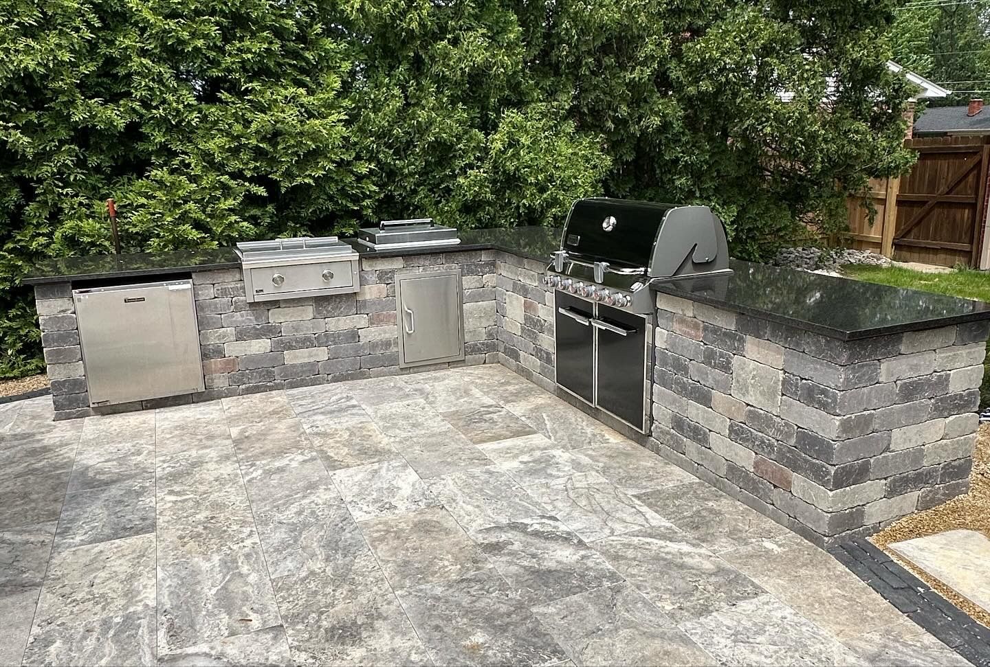 A large outdoor kitchen with a grill and a brick wall.