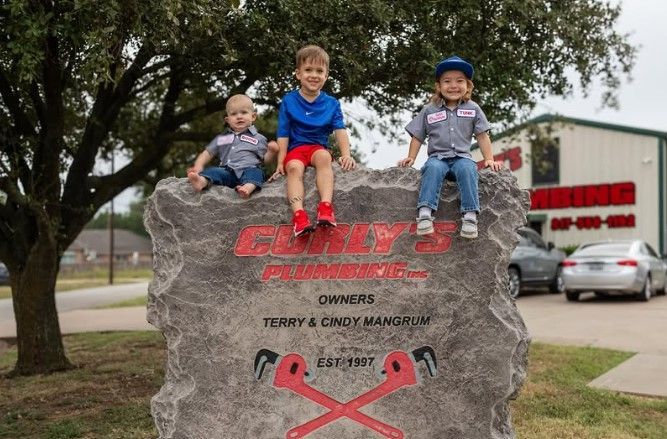Three young boys are sitting on top of a large rock.