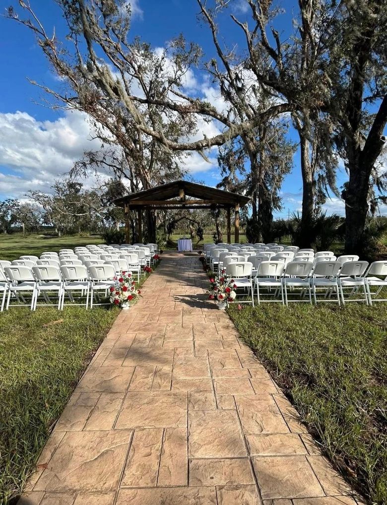 Wedding ceremony setup with white chairs lining a stone path to a gazebo under trees.