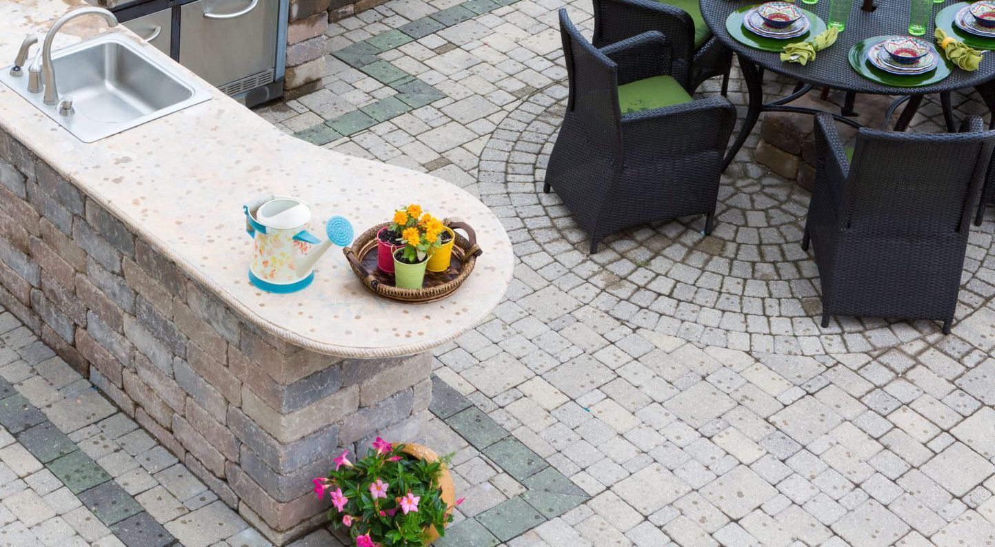 Outdoor kitchen with sink and countertop, patio with dining set and patterned brickwork.