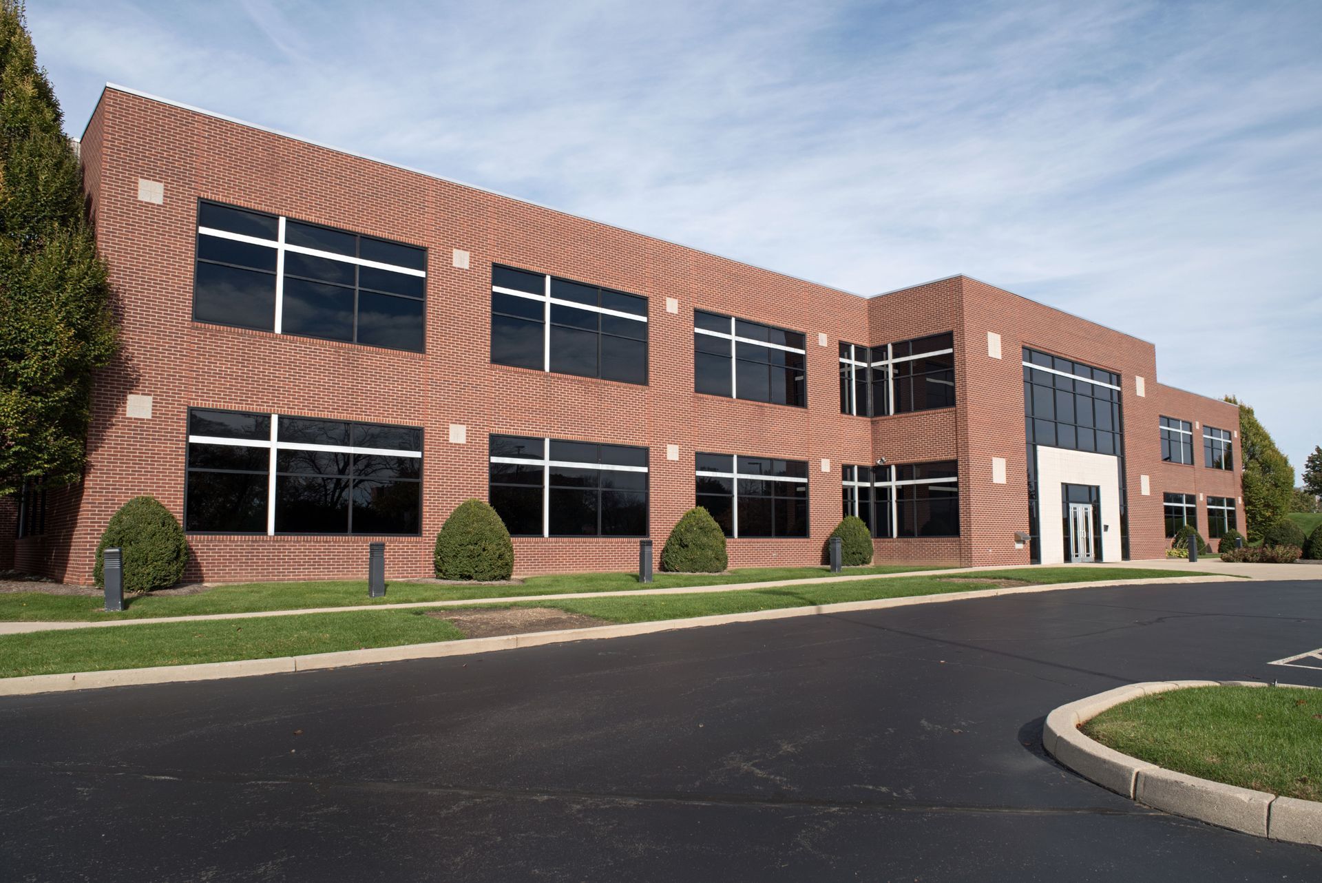 Red brick two-story office building with large windows. Landscaping in front, asphalt driveway.