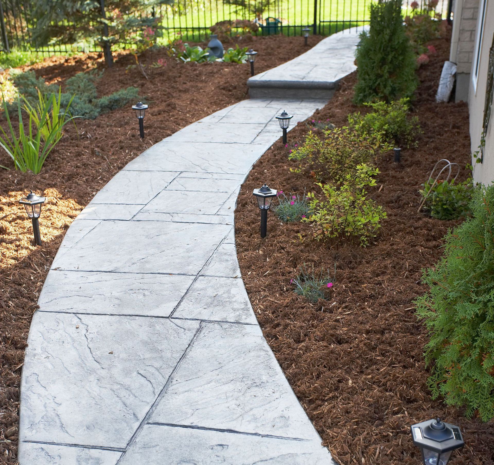 Stone pathway through a garden with mulch, plants, and solar lights.