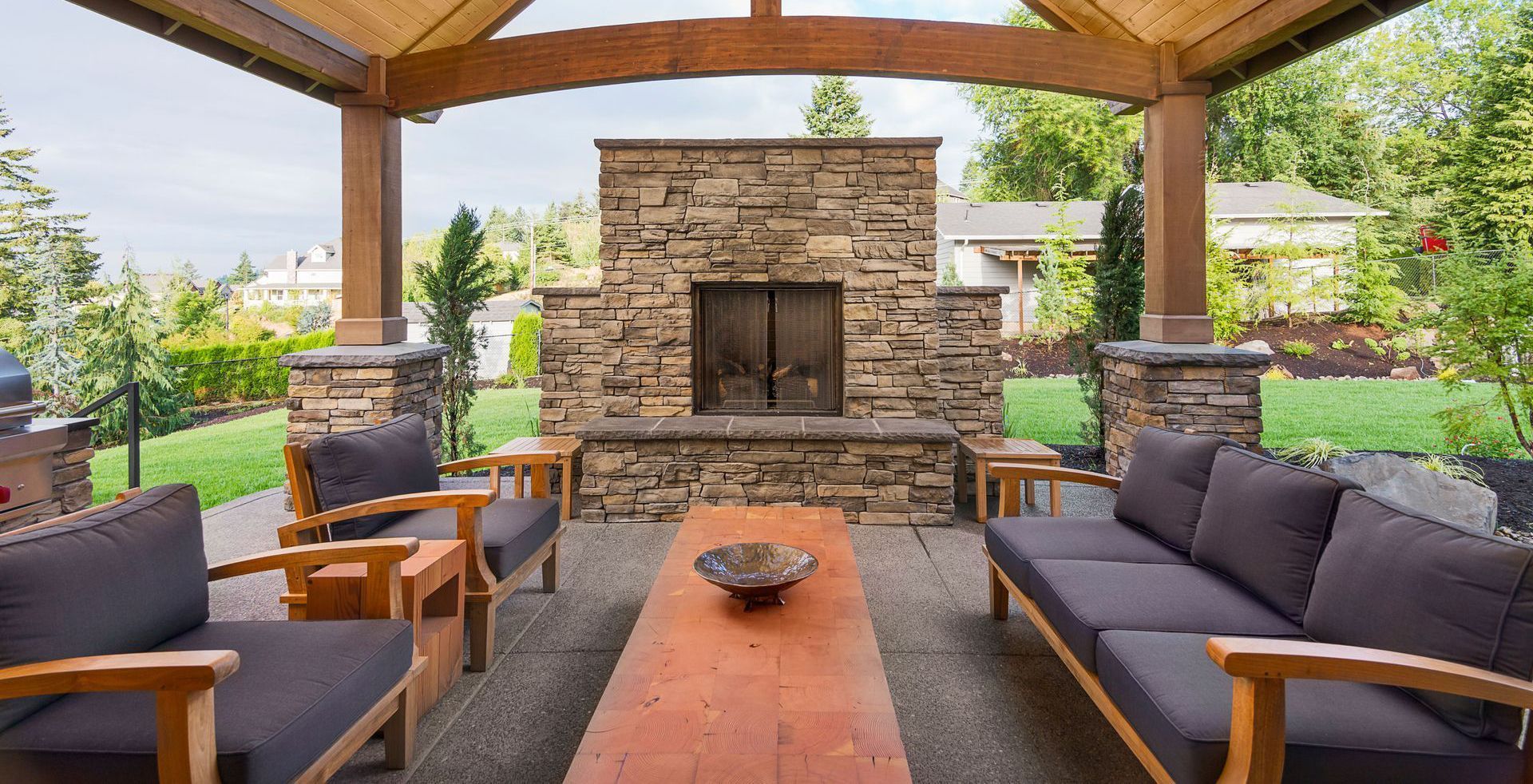 Outdoor living space with stone fireplace, wooden furniture, and covered patio.