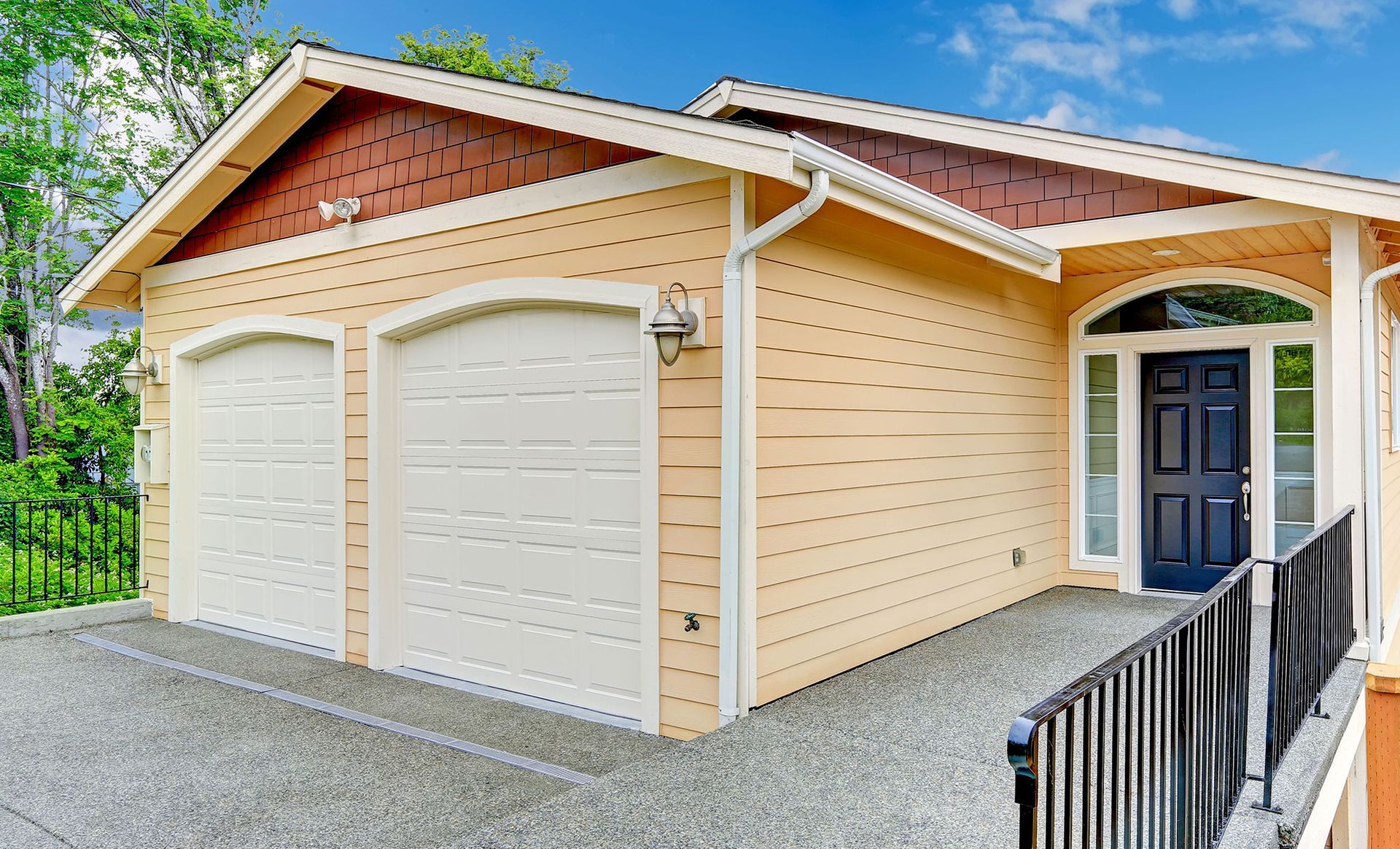 A yellow house with two garage doors and a dark blue front door. A ramp leads to the entrance.