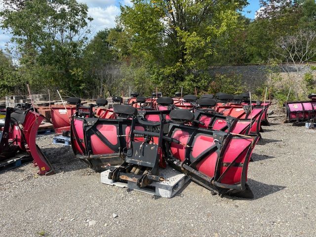 Red snow plows stacked outdoors on a sunny day.