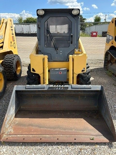 Yellow skid steer loader with a bucket, parked outside on a sunny day.