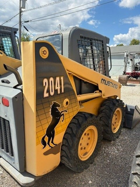 Yellow and gray Mustang 2041 skid steer loader with a horse logo, parked outdoors on a sunny day.