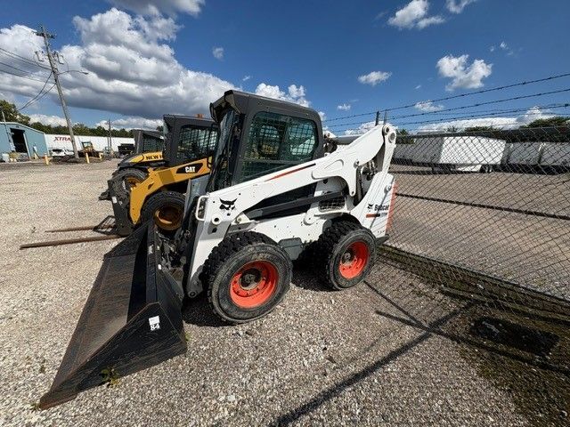 White Bobcat skid-steer loader with a black bucket parked outside near a fence on a cloudy day.