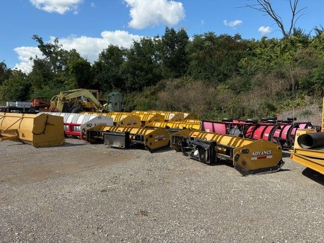 Outdoor storage yard with rows of yellow snow plows and barriers.