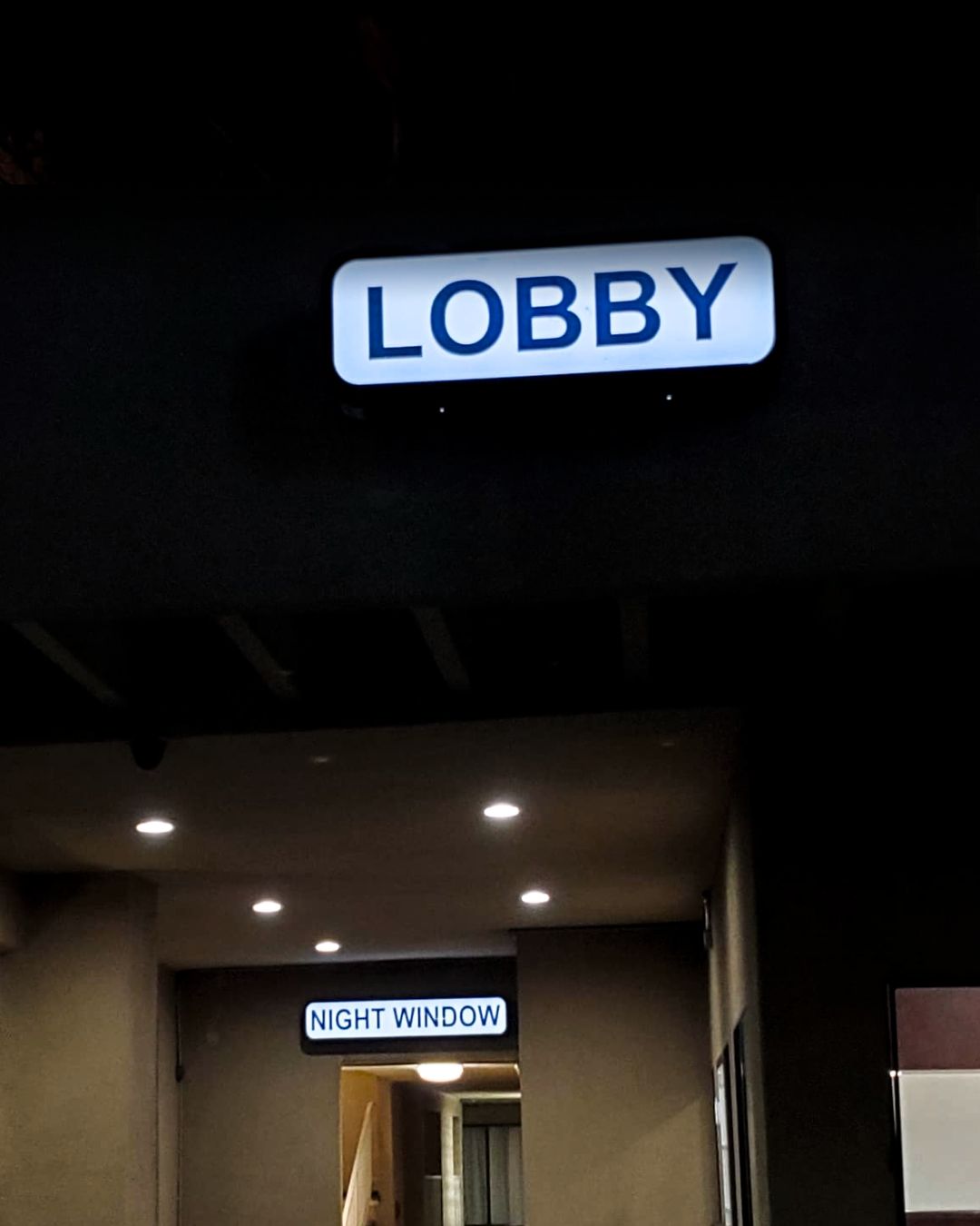Illuminated LOBBY sign above a doorway in a dark hallway, with a smaller sign below.