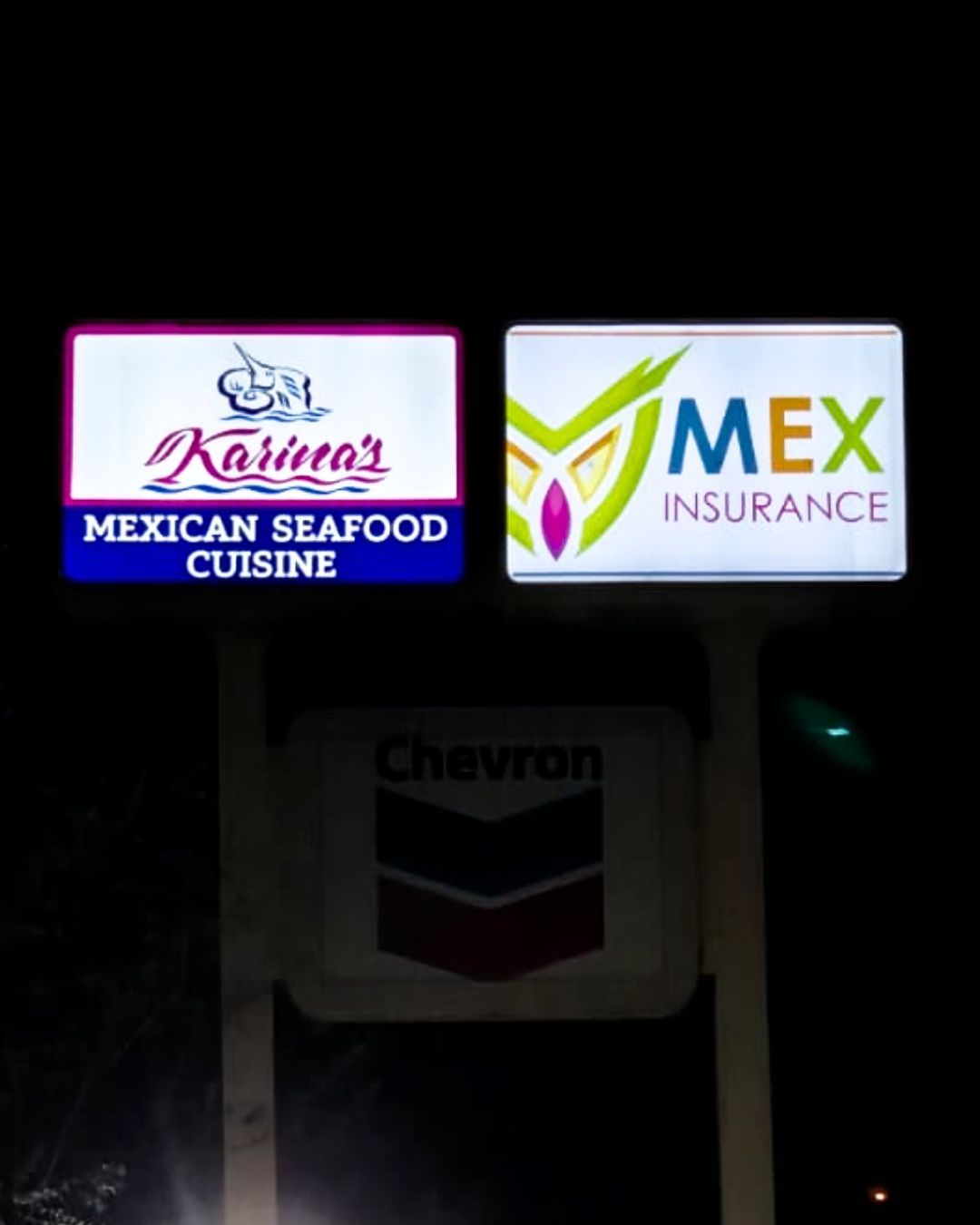 Illuminated Mexican Seafood Cuisine, MEX Insurance, and Chevron signs at night