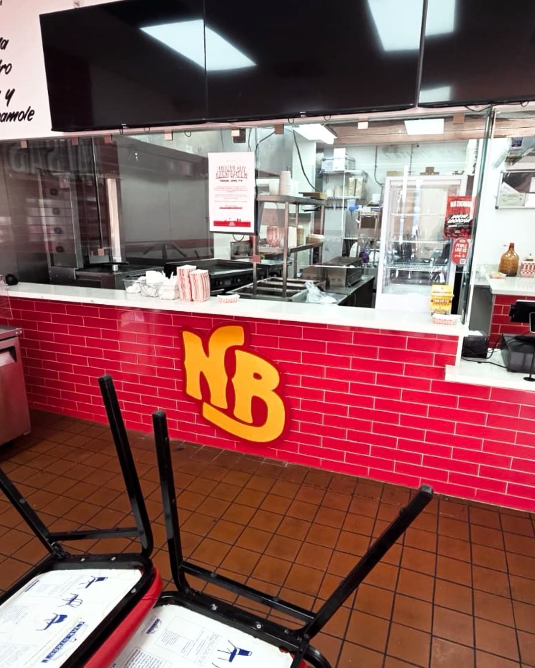 Fast-food counter with red tile front and yellow NB logo inside a bright cafeteria.