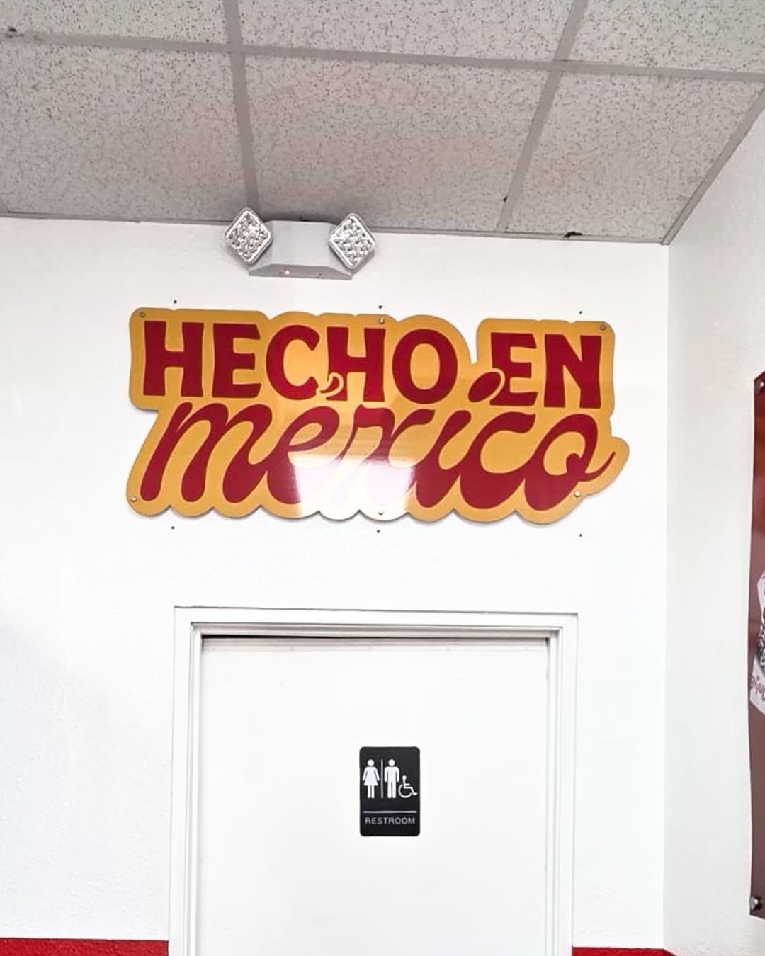 HECHO EN méxico sign in red and yellow above a white door with a restroom icon