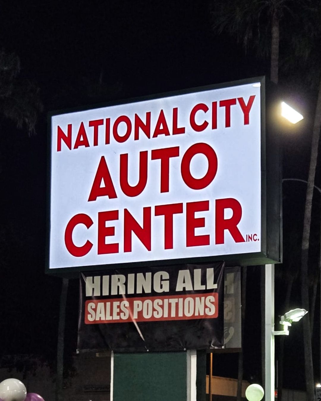 Sign for National City Auto Center with Hiring All Sales Positions below at night