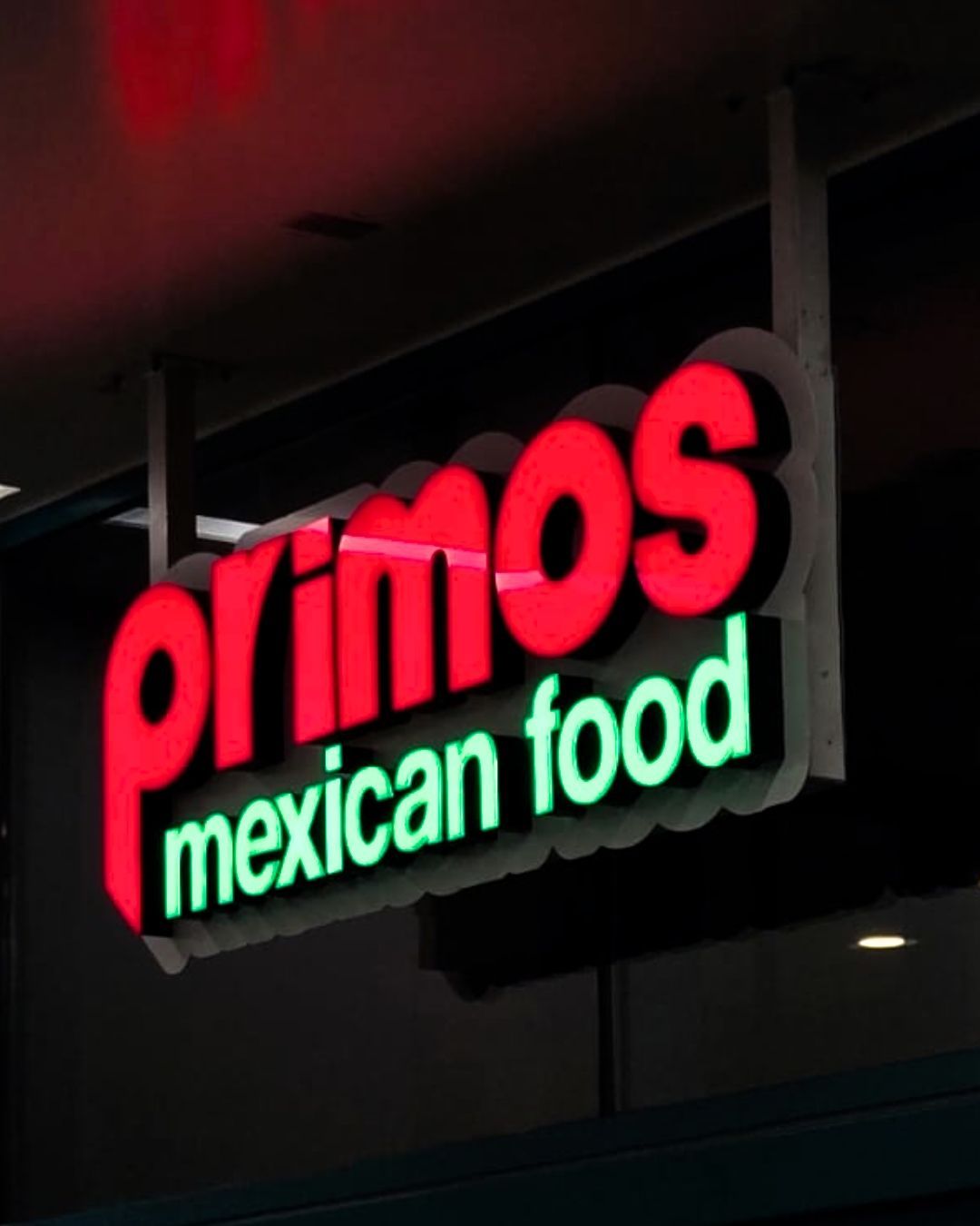 Neon sign reading Primos Mexican Food in red and green on a dark storefront