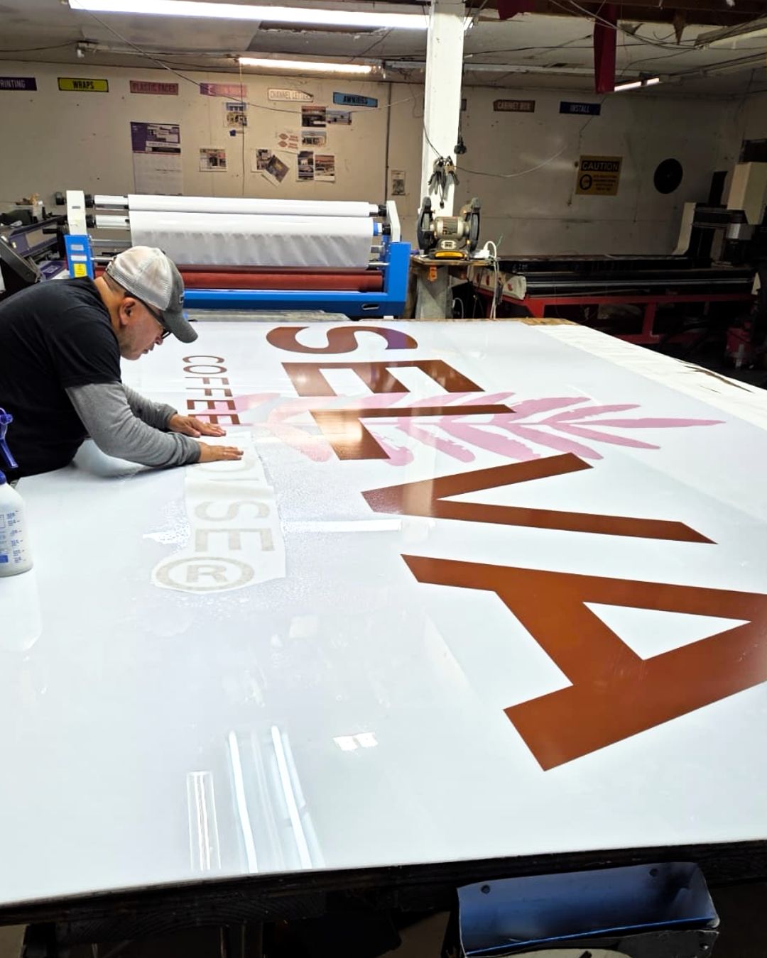 A worker applying large vinyl letters to a white sign in a print shop