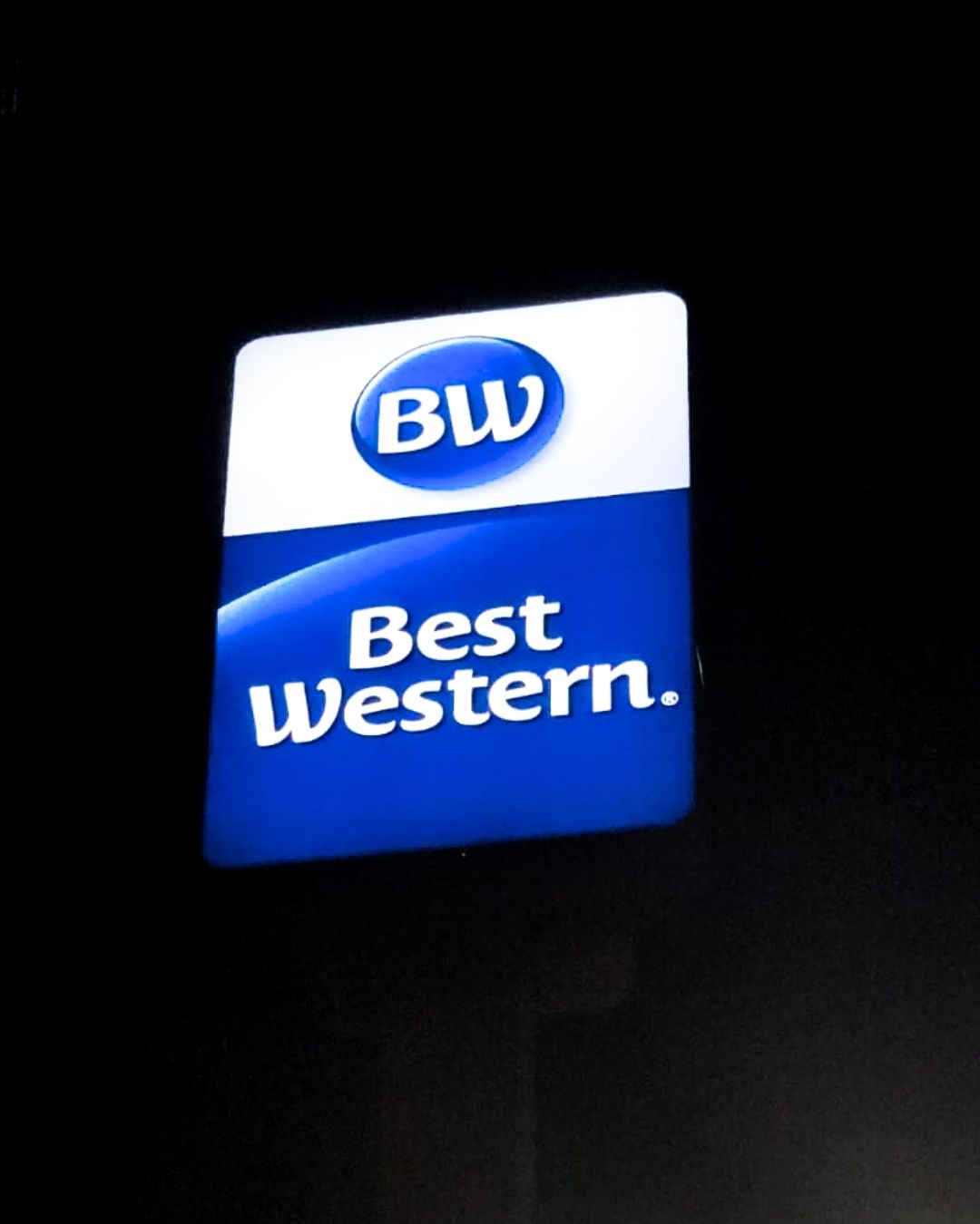 Illuminated Best Western hotel sign with blue and white logo on a dark background