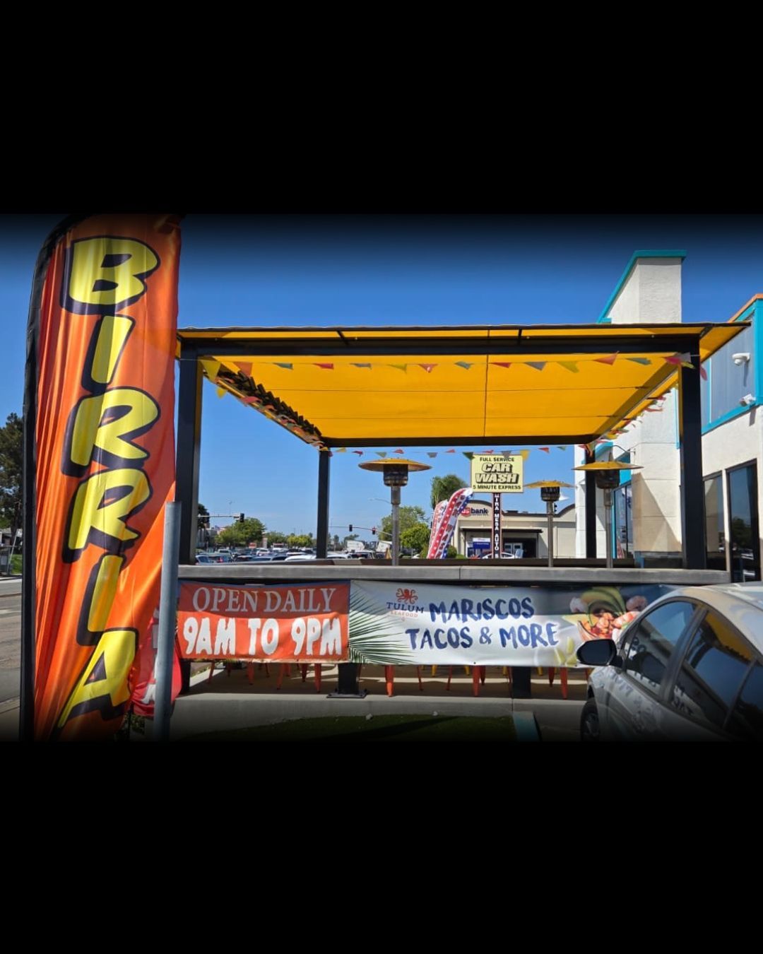Colorful roadside bar with a yellow canopy and mural-covered walls under a blue sky.